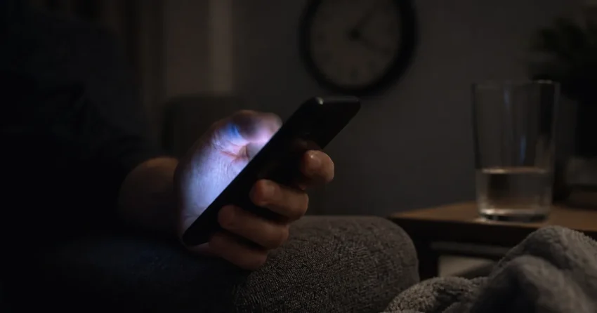En hand svepar på mobilskärmen i ett mörkt rum, symbol för algoritmstyrda flöden